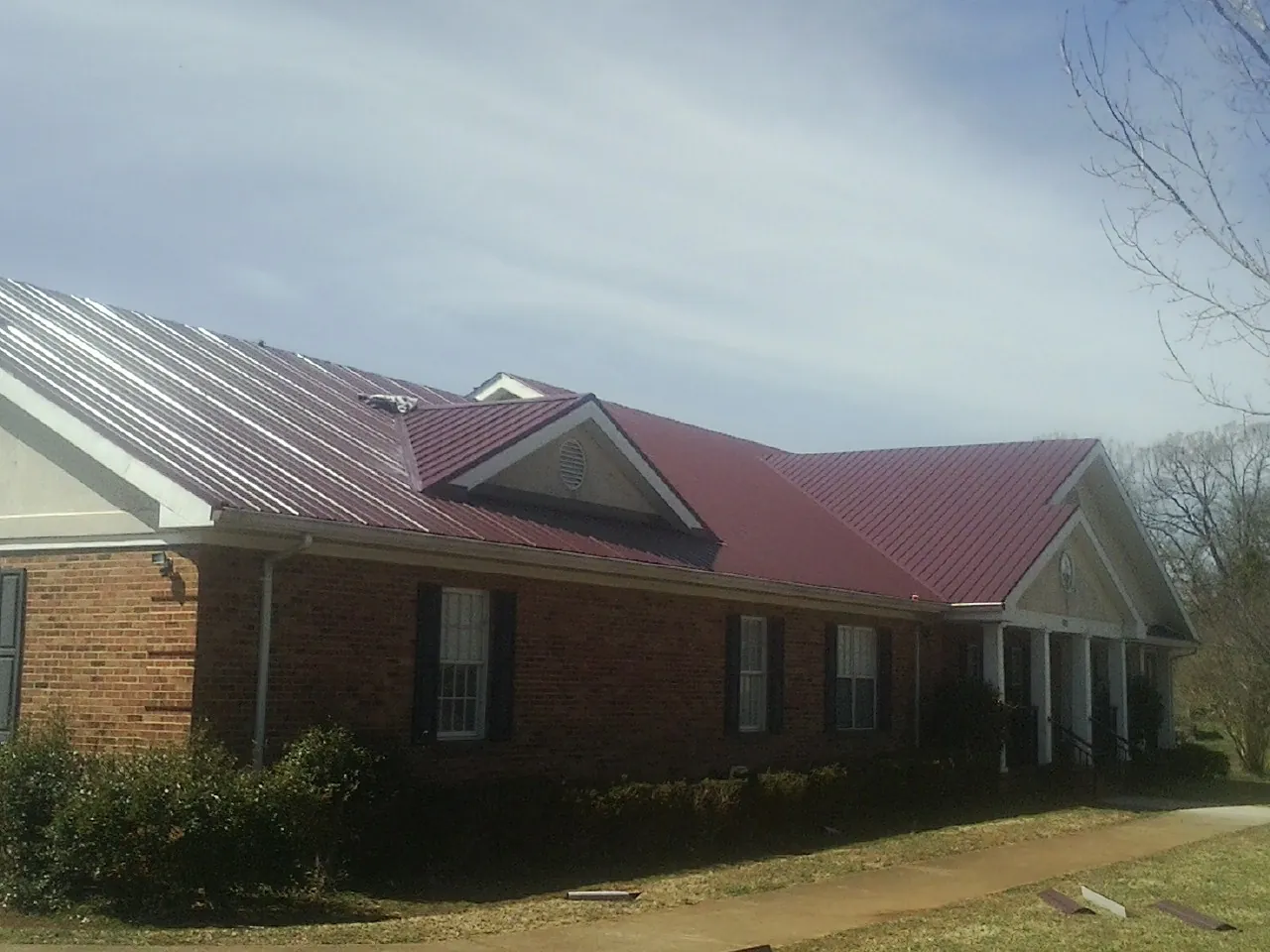 Red metal roof with gabled entries on a long brick building, from a Hail Damage Roof Repair job in Dacono