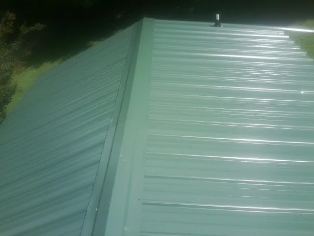 New green metal panels meeting at the ridge of a roof — Flat Roof Repair work by our crew in Dacono