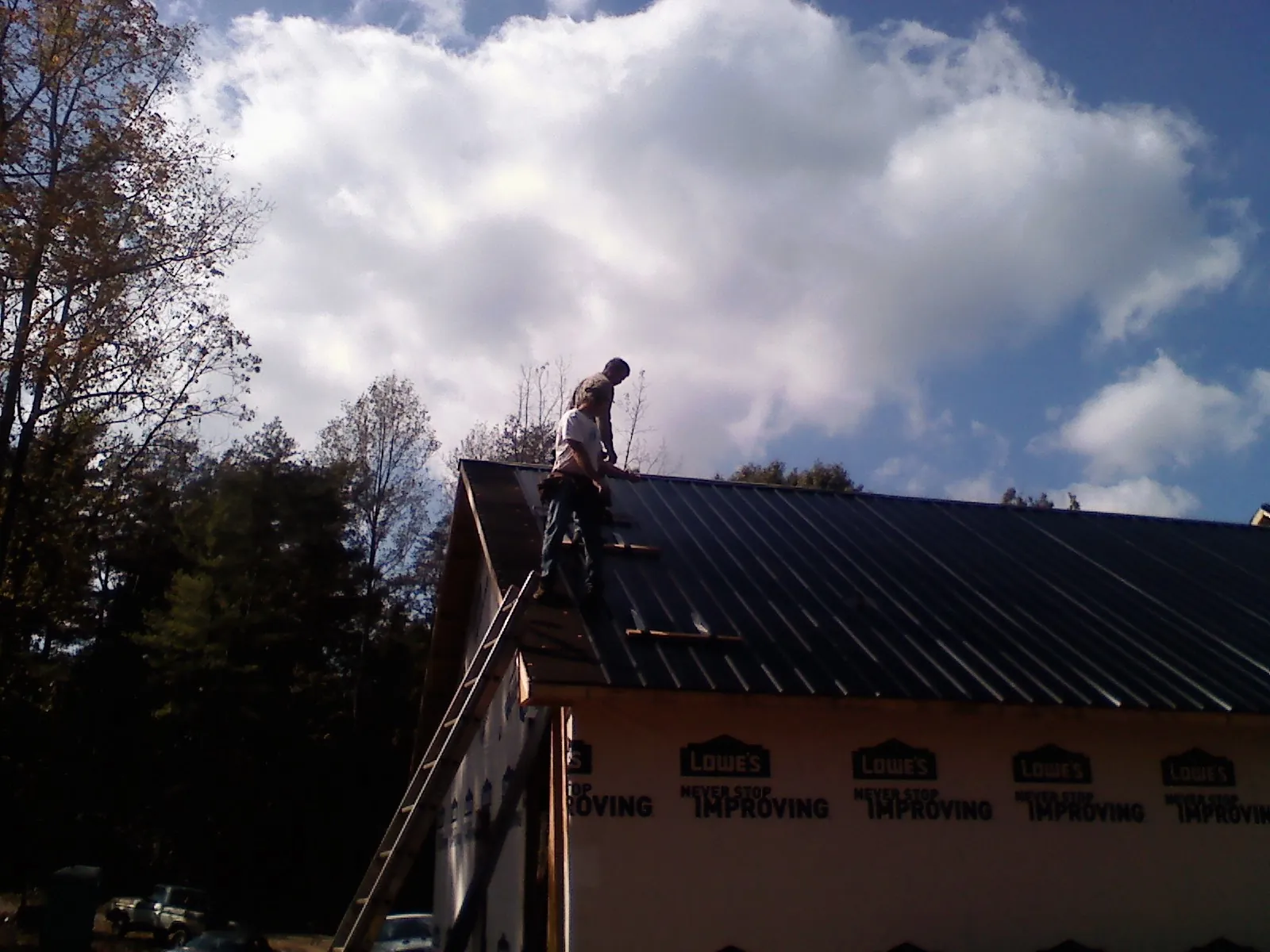 Roofer fastening dark metal panels high against a cloudy sky, from a Roof Inspection job in Dacono