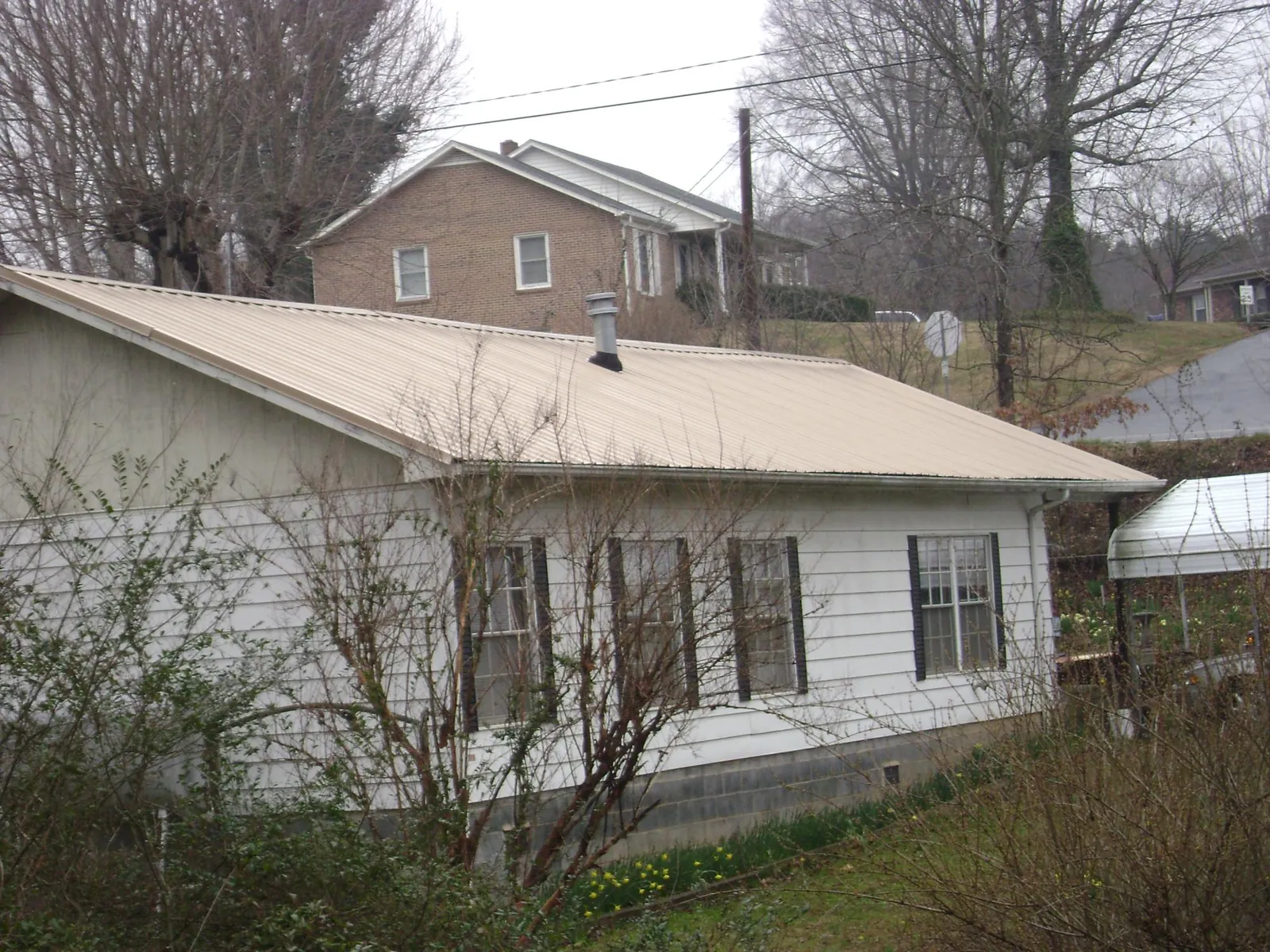 Tan metal roof on a white sided house set into a hillside — Commercial Roofing by Roofing Brothers in Dacono