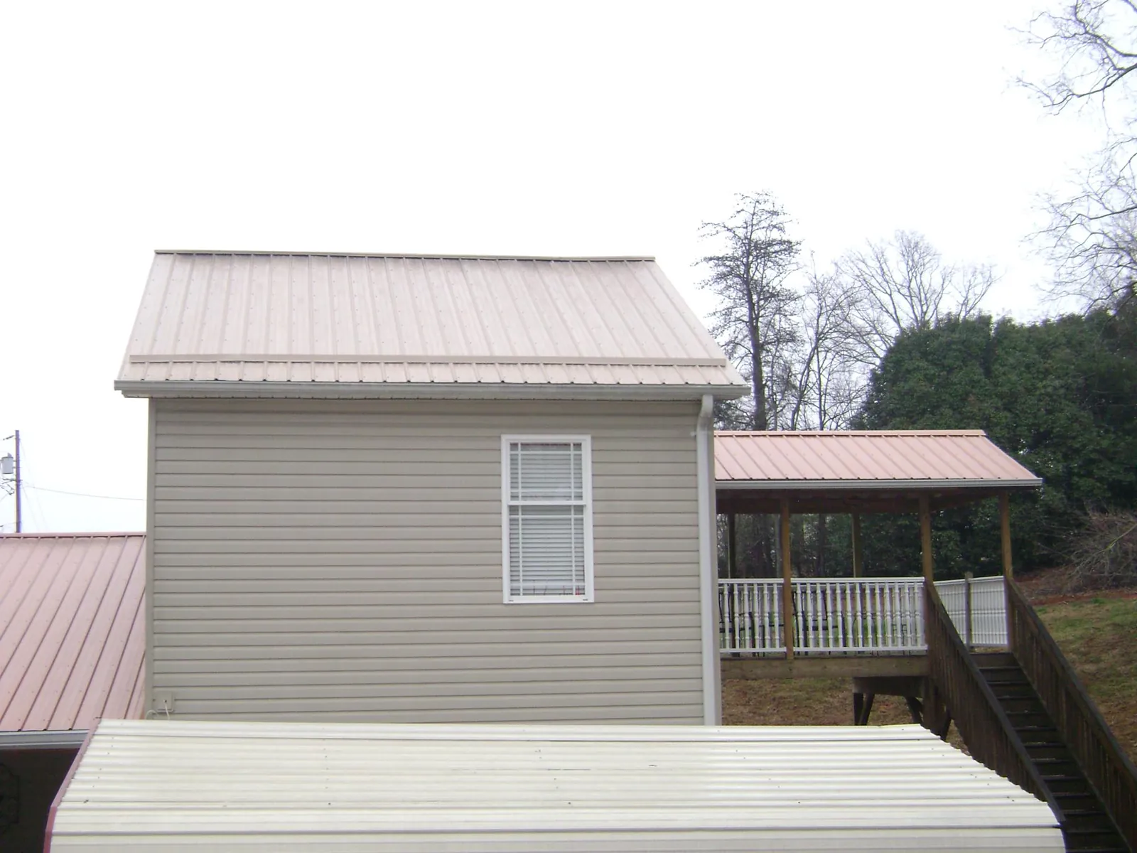 Tan metal roofs on a two story addition and attached porch, from a Roof Replacement job in Dacono